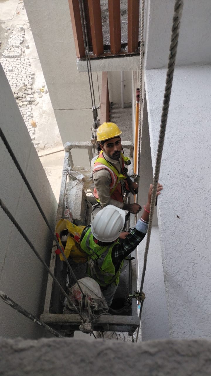 Safety-equipped workers installing vertical utility pipework from a suspended platform