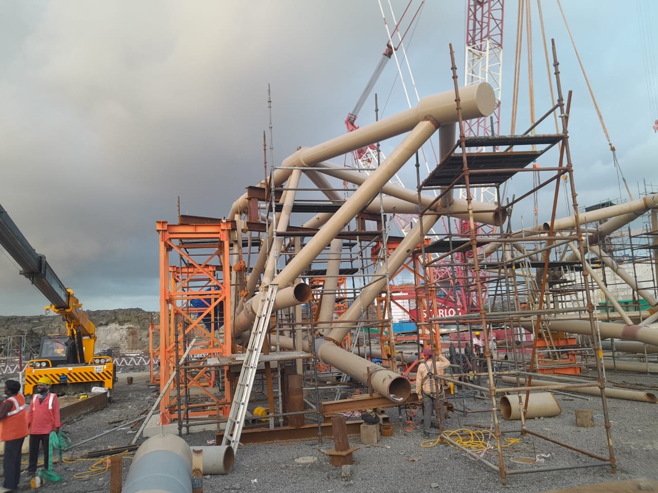 Large steel framework under construction with cranes and scaffolding