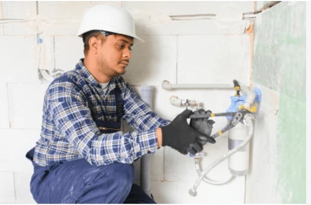 Plumber in safety helmet tightening a wall-mounted filter and valve assembly